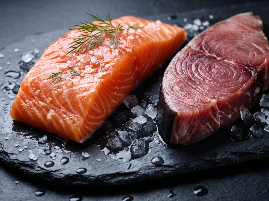 Fresh wild salmon fillet rich in omega-3 next to high-mercury pelagic predatory fish steak on black slate with crushed ice