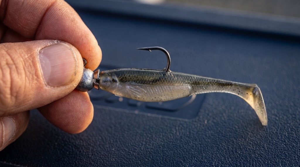 Close-up macro demonstration of perfectly rigged soft plastic swimbait on ball jig head with barbed collar