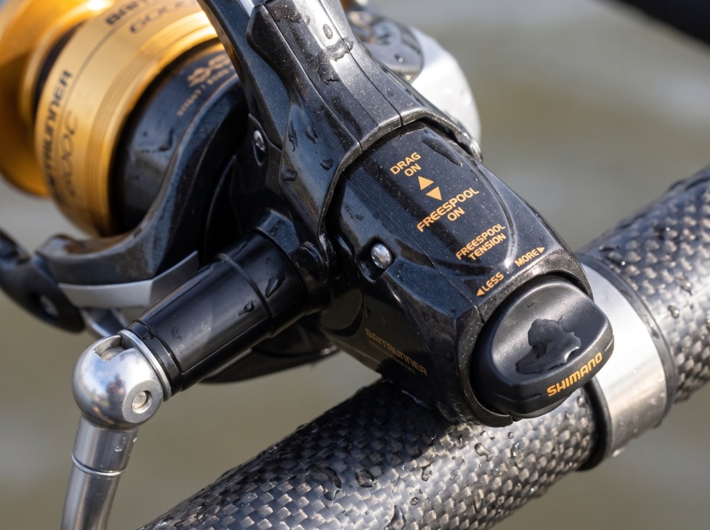 Macro detail of the Shimano Baitrunner D rear lever and tension knob dial on a carbon fishing rod handle
